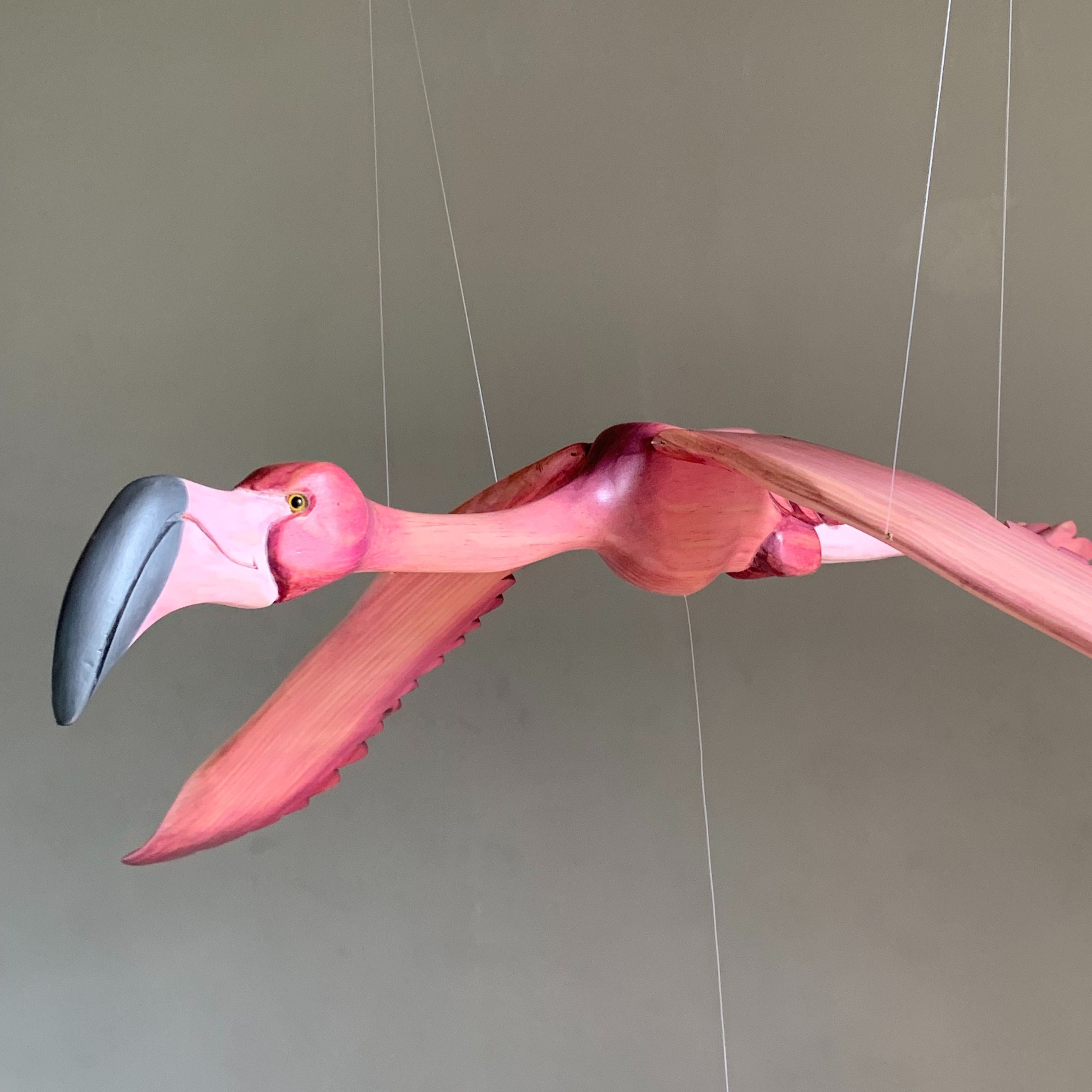 Close-up of a hand-carved wooden flamingo mobile showing its sculpted beak, painted feathers and suspension cords