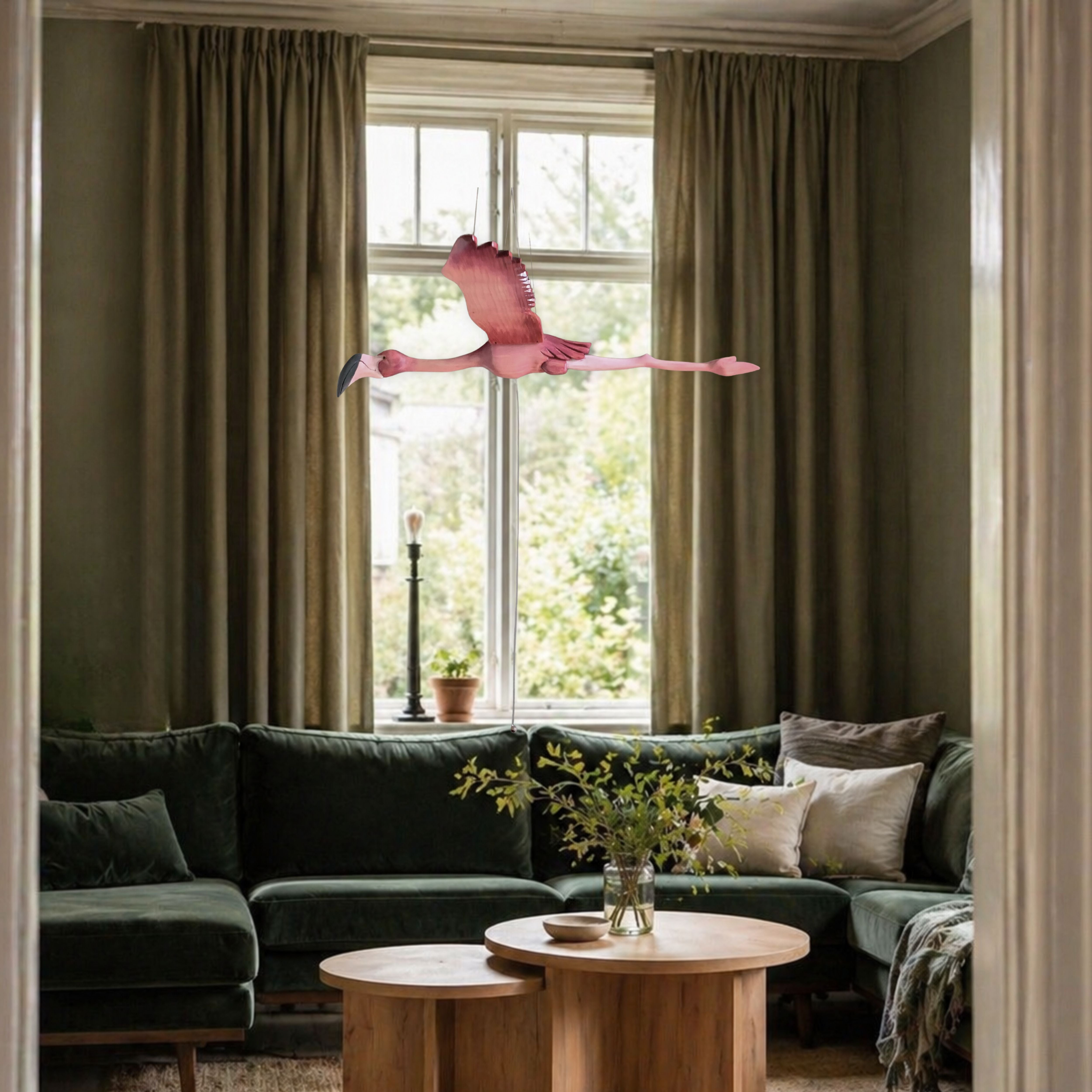 Hand-carved wooden flamingo mobile in flight above a dark green velvet sofa in an elegant living room