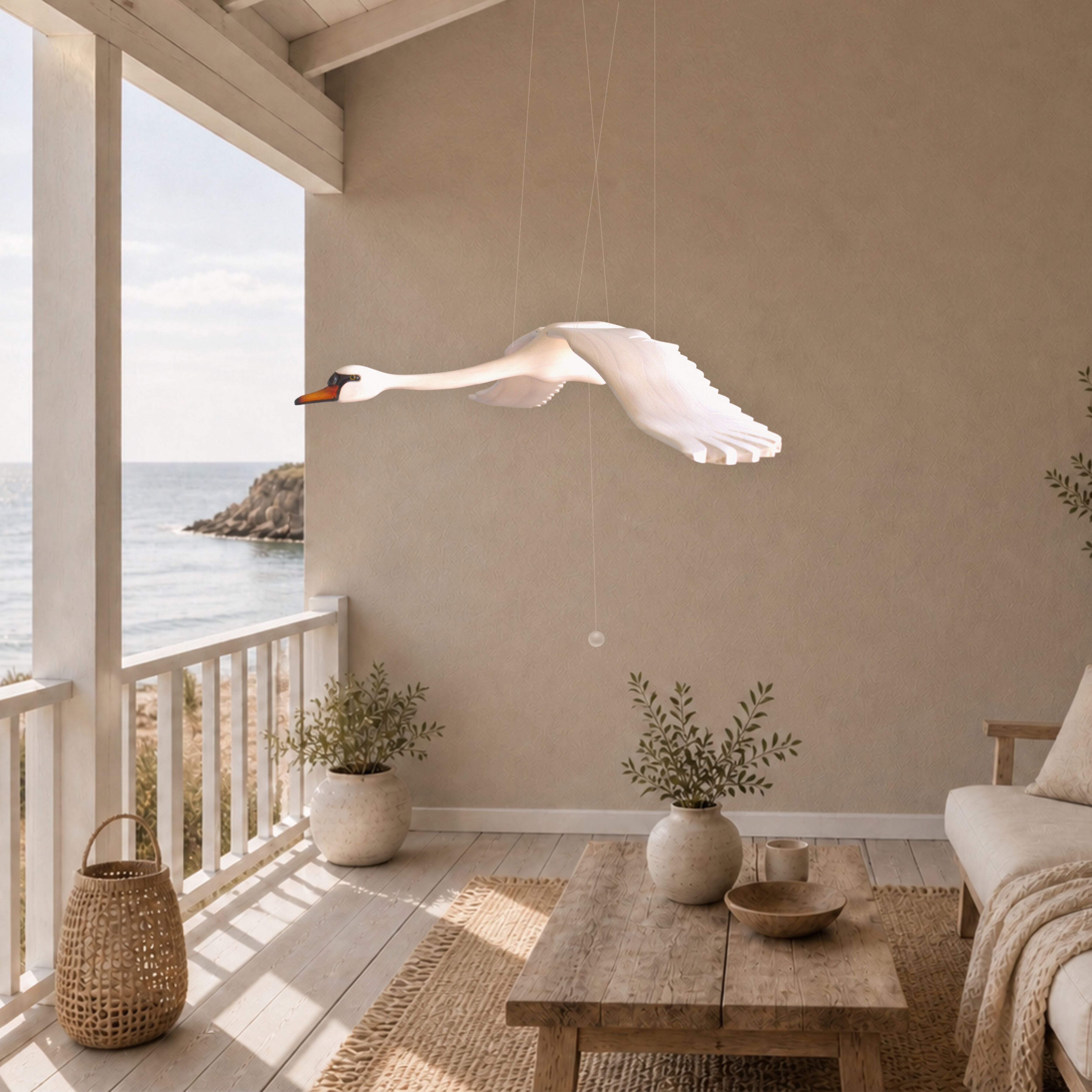 Hand-carved wooden swan mobile in flight on a light coastal veranda overlooking the sea