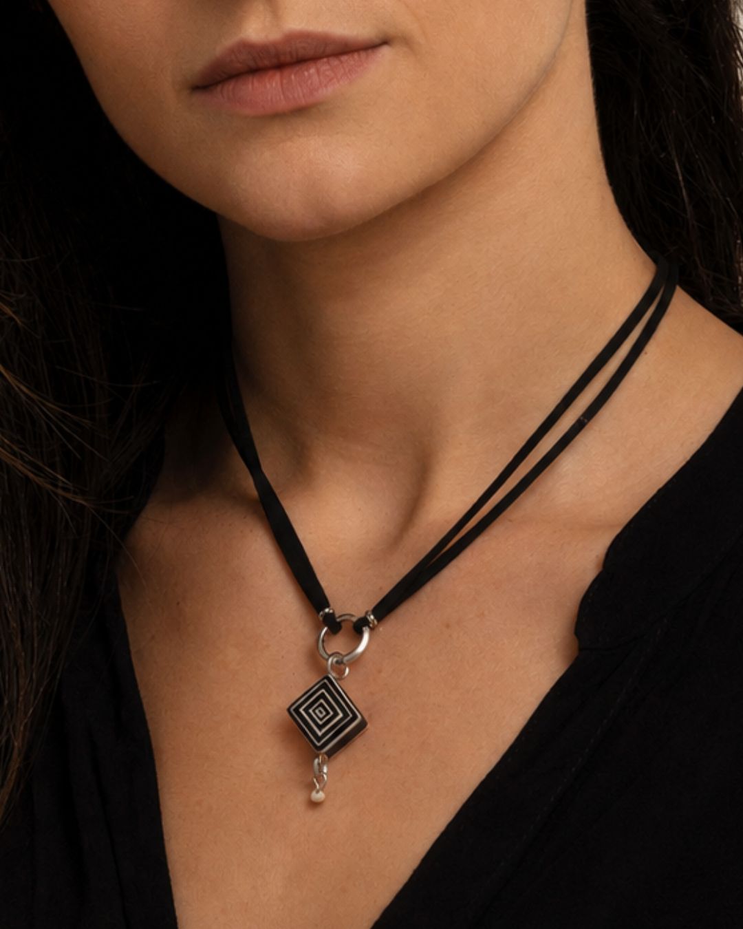 Close-up of a handcrafted petite geometric ostrich eggshell pendant showing its layered contemporary design and black suede cord.