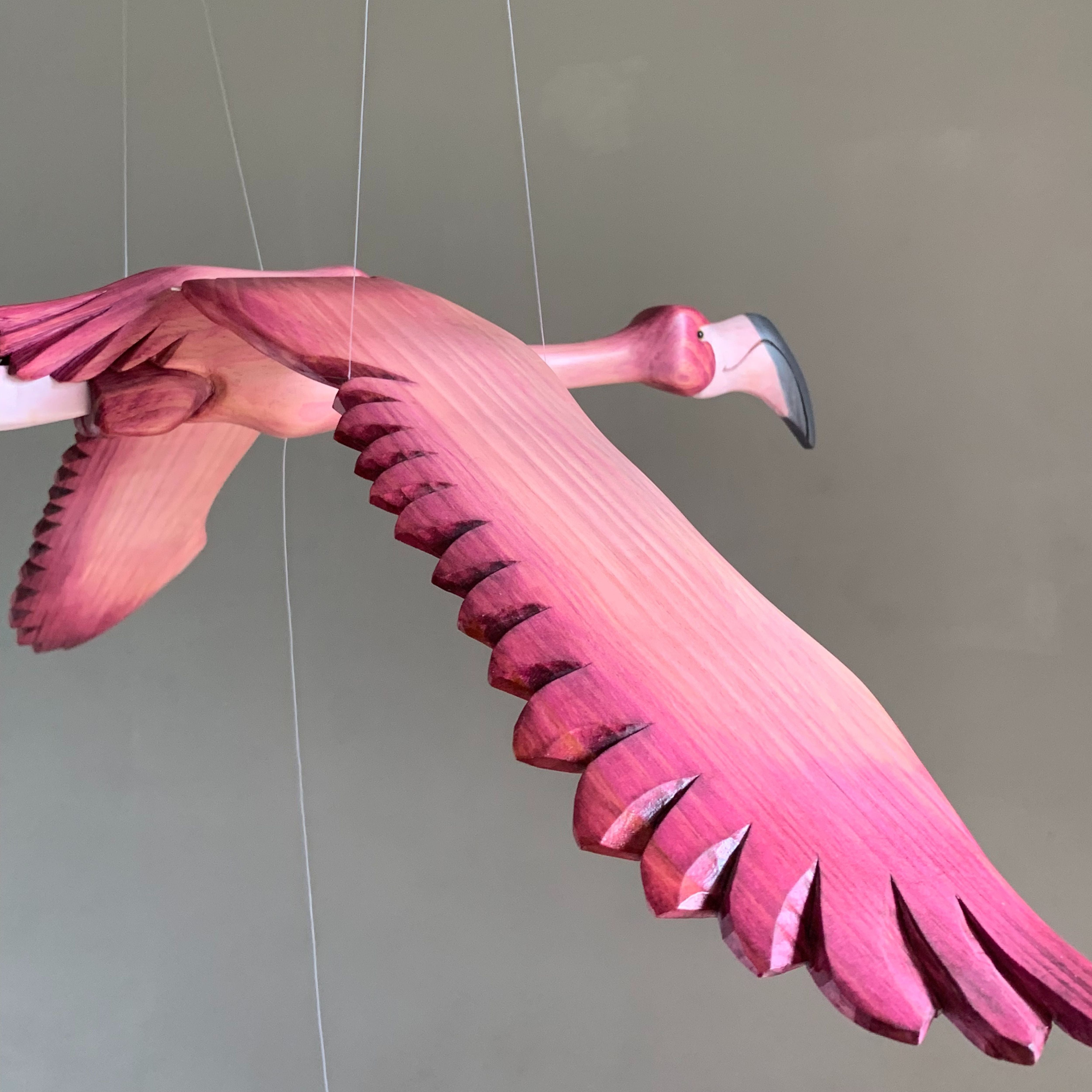 Close-up of a hand-carved wooden flamingo mobile showing the detailed carving and painted feathers on the wings