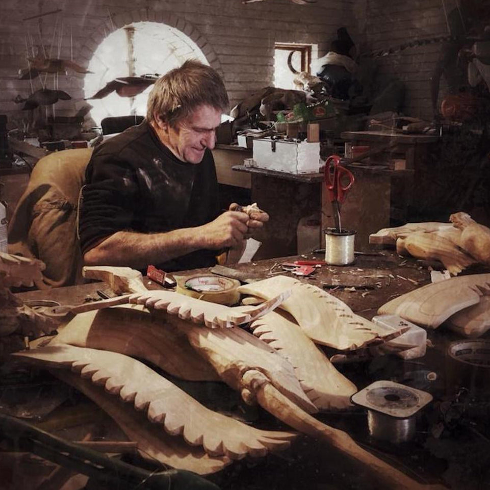 Wood carver working on a wooden flamingos in a workshop with various tools and materials.
