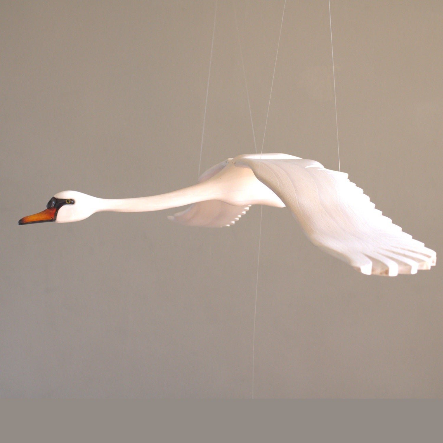 Hand-carved swan mobile close-up against a grey wall background