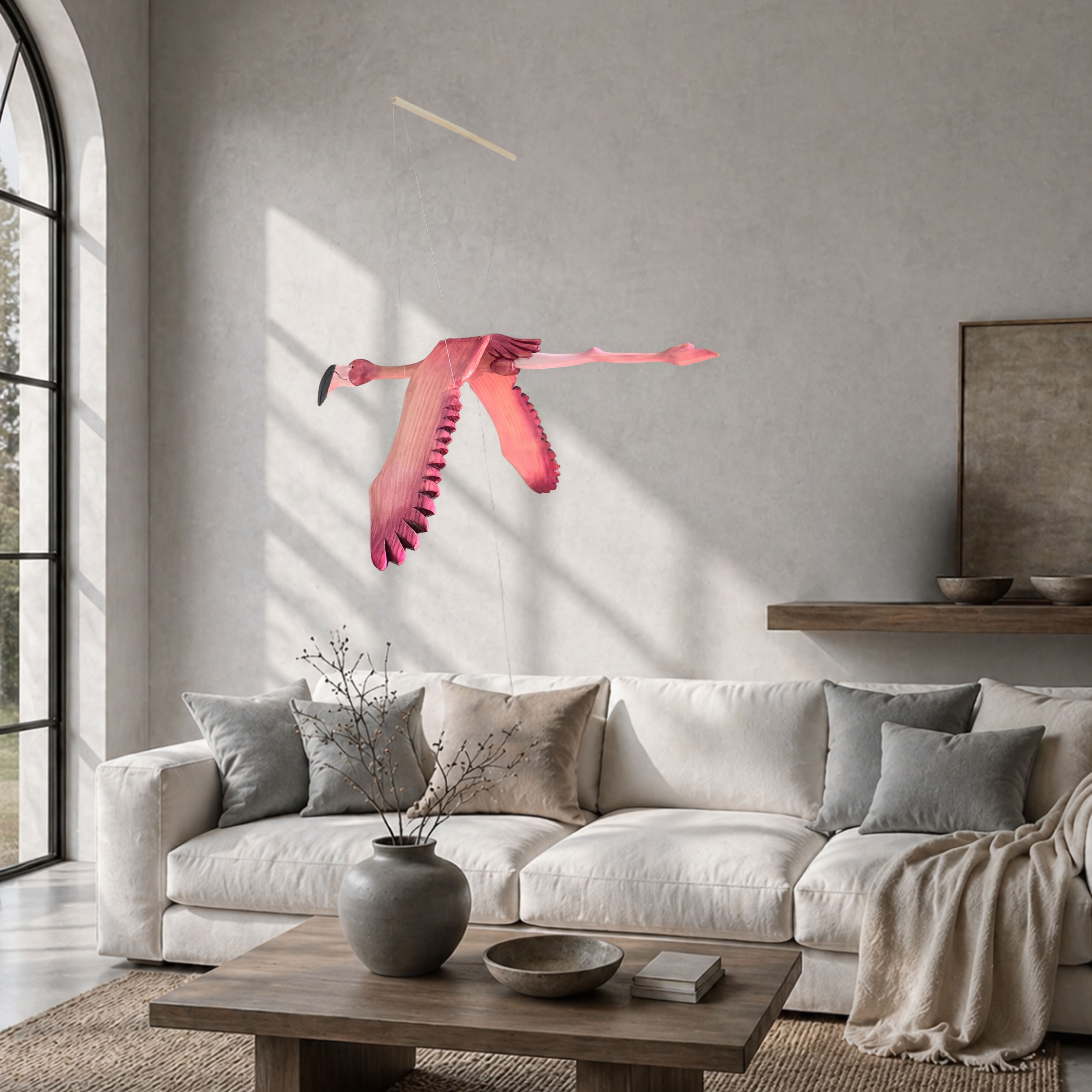Hand-carved wooden flamingo mobile in flight above a light Japandi-style living room with natural wood and neutral tones