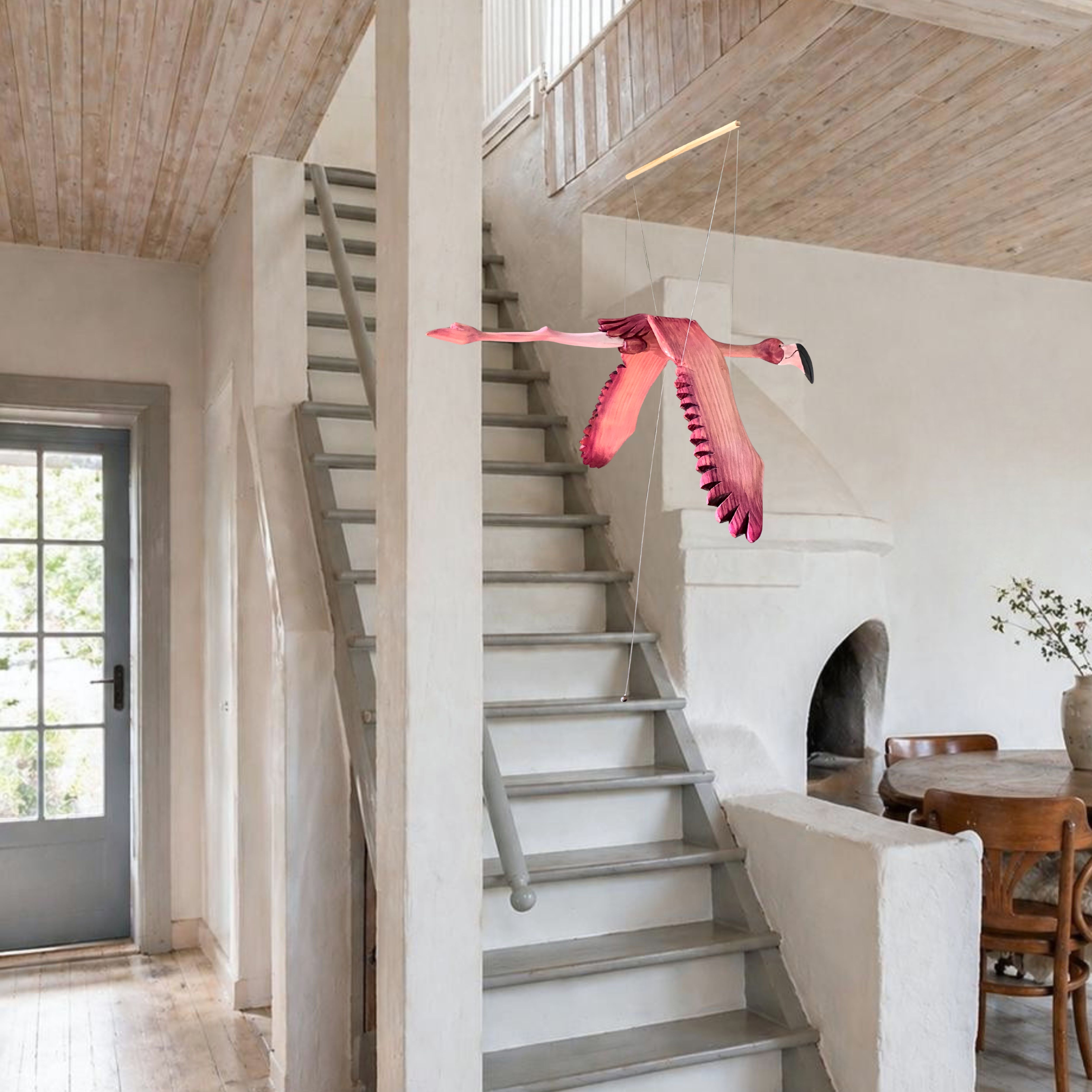 Hand-carved wooden flamingo mobile in flight beside a staircase in a light rustic double-volume interior
