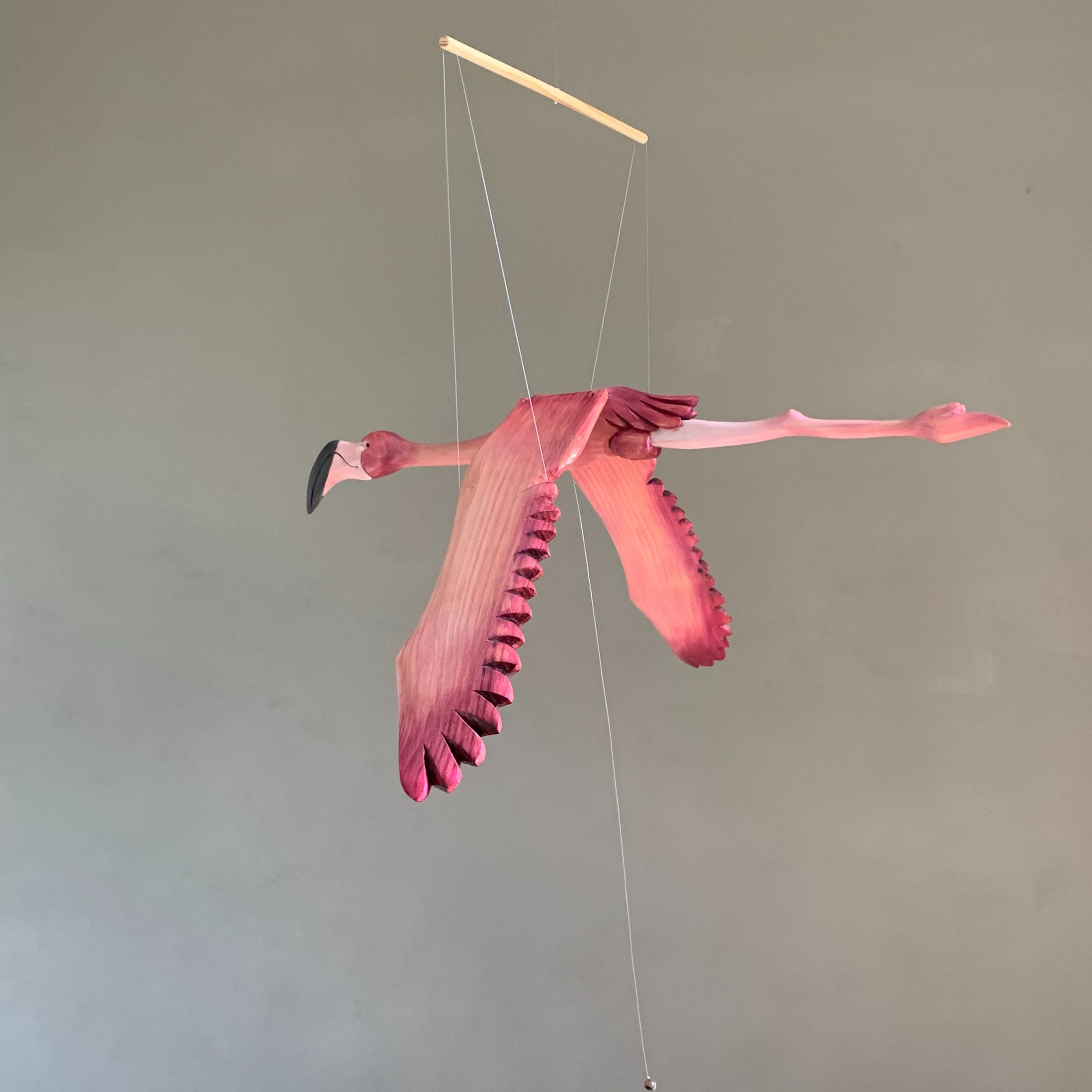 Hand-carved wooden flamingo mobile hanging from a wooden dowel with visible suspension cords