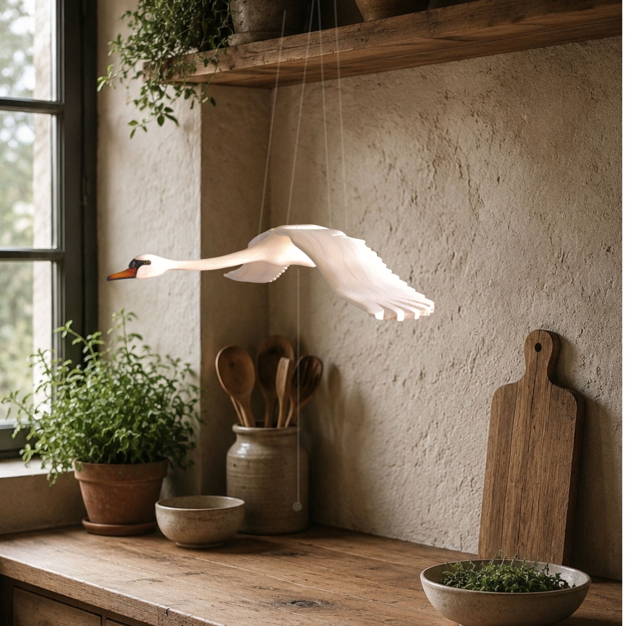Hand-carved swan mobile in a rustic country kitchen setting with wooden shelves and plants.